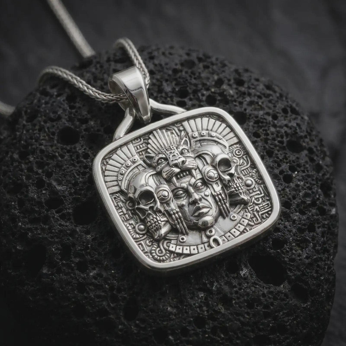 Polished sterling silver Aztec pendant displayed on dark volcanic stone, highlighting the jaguar headdress, skull motifs, detailed warrior face, feathers, and geometric Mexica-inspired ornament.
