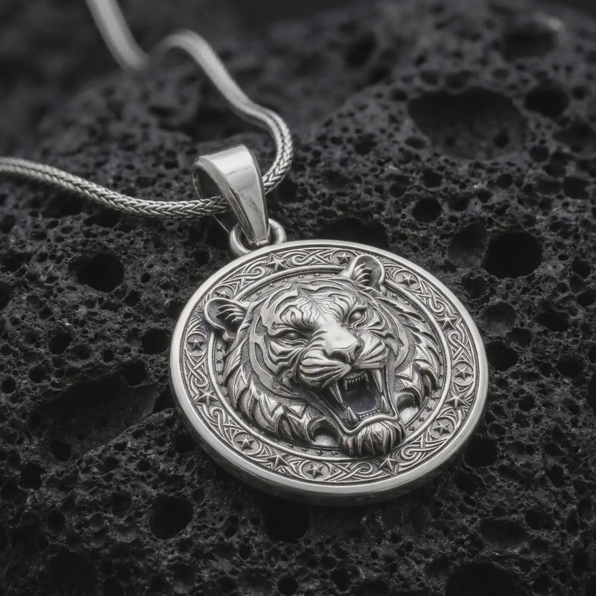 Polished sterling silver tiger head necklace displayed on dark volcanic stone, highlighting the roaring expression, sculpted stripes, fangs, and decorative medallion frame.