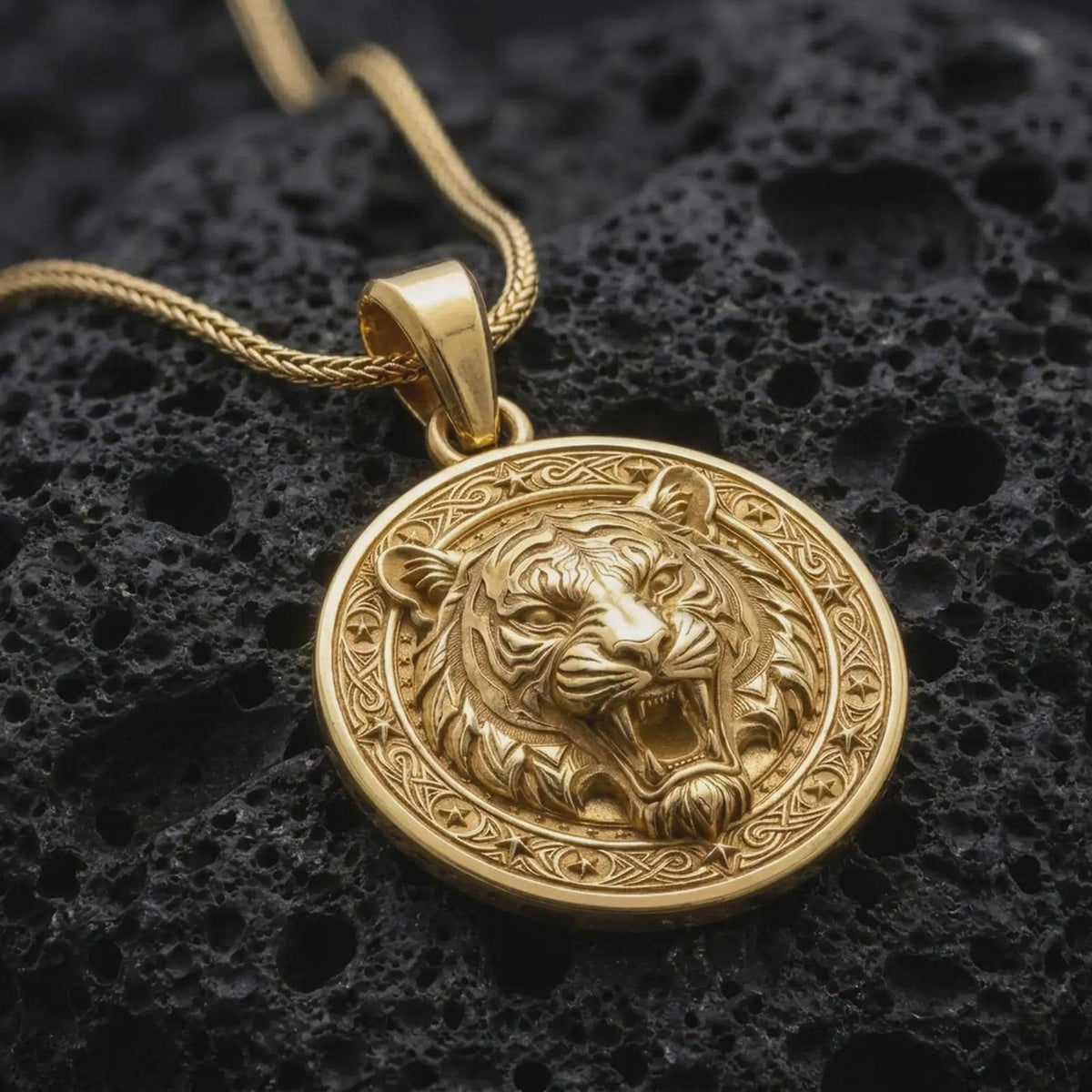 Gold plated roaring tiger pendant resting on black volcanic rock, featuring a fierce tiger face, detailed fur, prominent fangs, and an ornamental circular border.
