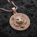 Load image into Gallery viewer, Rose gold plated tiger head necklace displayed on textured volcanic stone, showcasing the roaring tiger, sculpted stripes, sharp teeth, and detailed round medallion design.
