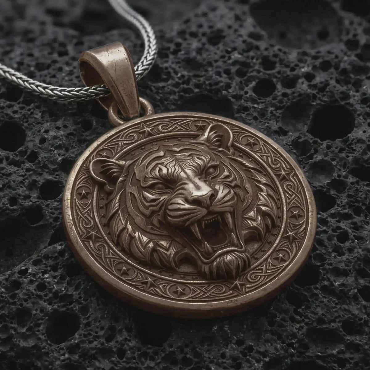 Bronze roaring tiger pendant on black volcanic rock, featuring a detailed tiger head, open mouth, sharp fangs, striped fur, and ornate circular border.