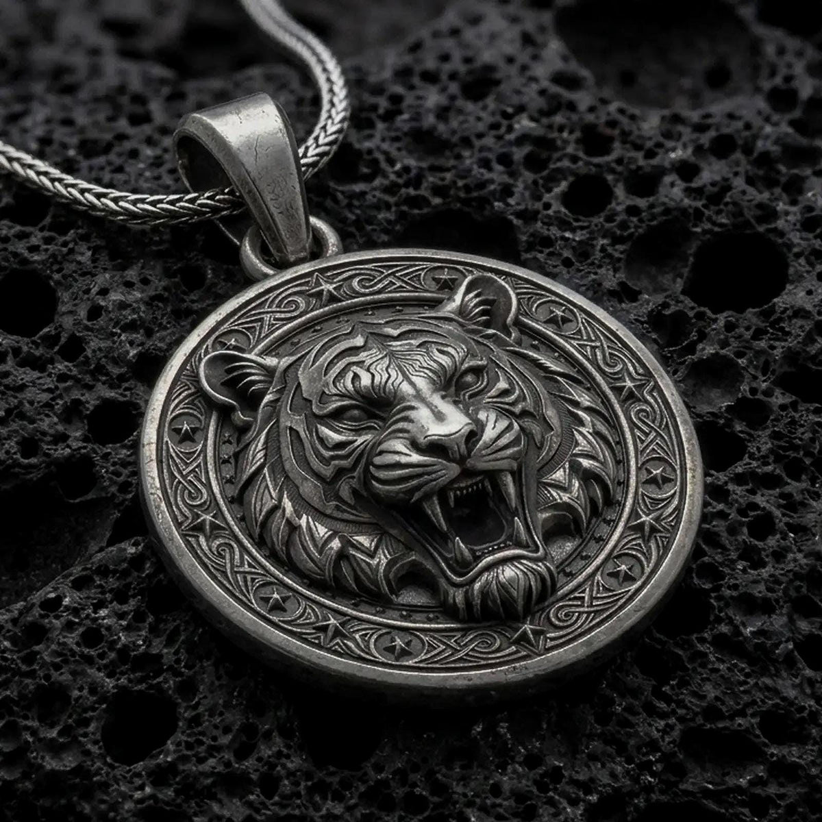 Oxidized sterling silver roaring tiger pendant on black volcanic rock, featuring a detailed tiger head, open mouth, sharp fangs, striped fur, and ornate circular border.