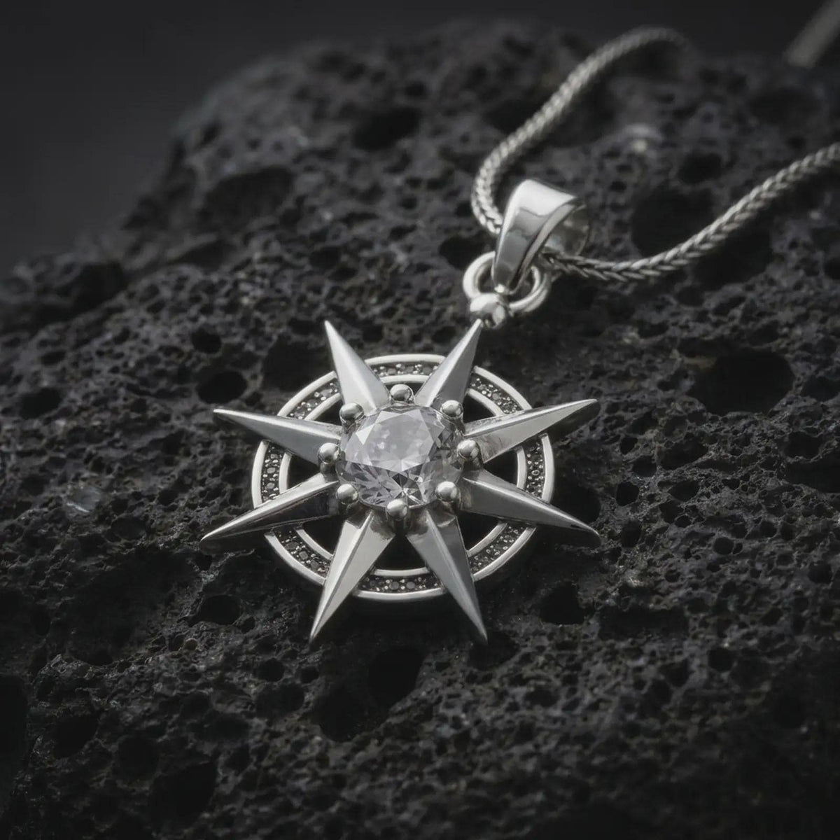 Polished sterling silver BG3 Gale charm displayed on dark volcanic stone, highlighting the sharp star points, circular frame, and sparkling faceted centerpiece.