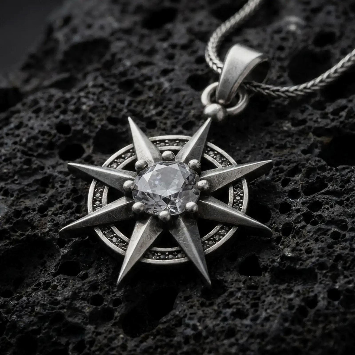 Oxidized sterling silver Gale's Earring inspired pendant on black volcanic rock, featuring an eight-point starburst design and a large clear faceted center stone.