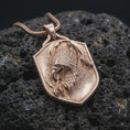 Load image into Gallery viewer, Rose gold plated eagle necklace displayed on textured volcanic stone, showcasing the sculpted eagle head, layered feathers, talon details, and distinctive shield pendant shape.
