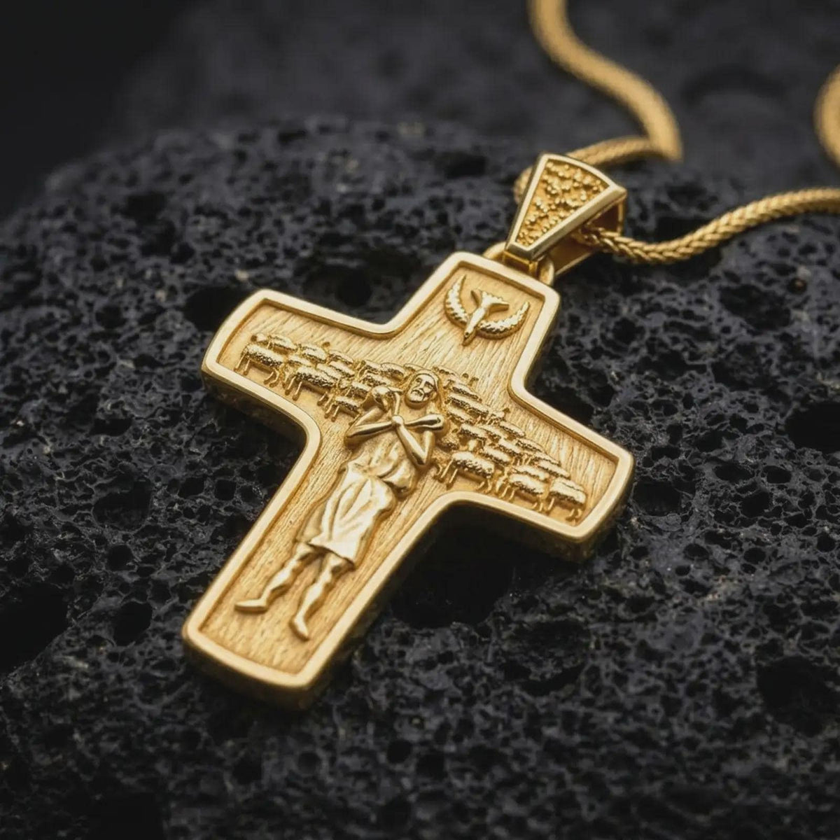 A gold plated Pope Francis cross necklace rests on rugged volcanic rock, showcasing the Good Shepherd carrying a sheep, surrounding flock, dove above, and symbolic Catholic religious design in a luxury macro studio close-up.