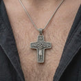 Load image into Gallery viewer, An oxidized sterling silver Pope Francis cross pendant is worn on the chest, displaying the Good Shepherd carrying a sheep, surrounding flock, dove motif, and substantial Christian cross profile in a close-up lifestyle photograph.
