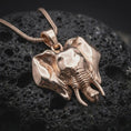 Load image into Gallery viewer, Rose gold plated elephant necklace displayed on textured volcanic stone, showcasing the sculpted elephant face, curved tusks, detailed trunk, and large symmetrical ears.
