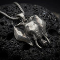Load image into Gallery viewer, Oxidized sterling silver elephant head pendant on black volcanic rock, featuring large sculpted ears, detailed tusks, expressive eyes, and a dimensional curled trunk.
