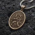 Load image into Gallery viewer, A Bronze sterling silver St. Christopher pendant rests on dark volcanic rock, featuring Saint Christopher carrying the Christ Child across flowing water with halo details and raised Catholic religious relief in a macro studio close-up.
