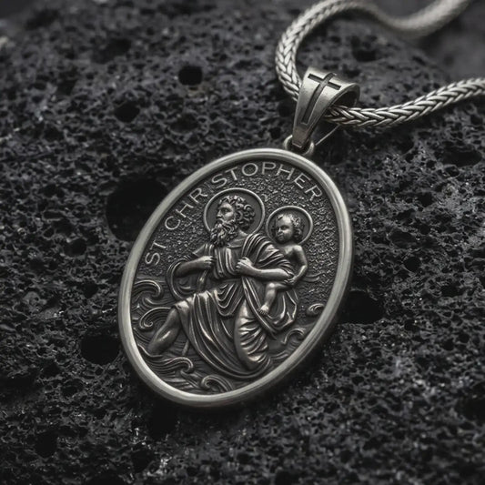 An oxidized sterling silver St. Christopher pendant rests on dark volcanic rock, featuring Saint Christopher carrying the Christ Child across flowing water with halo details and raised Catholic religious relief in a macro studio close-up.