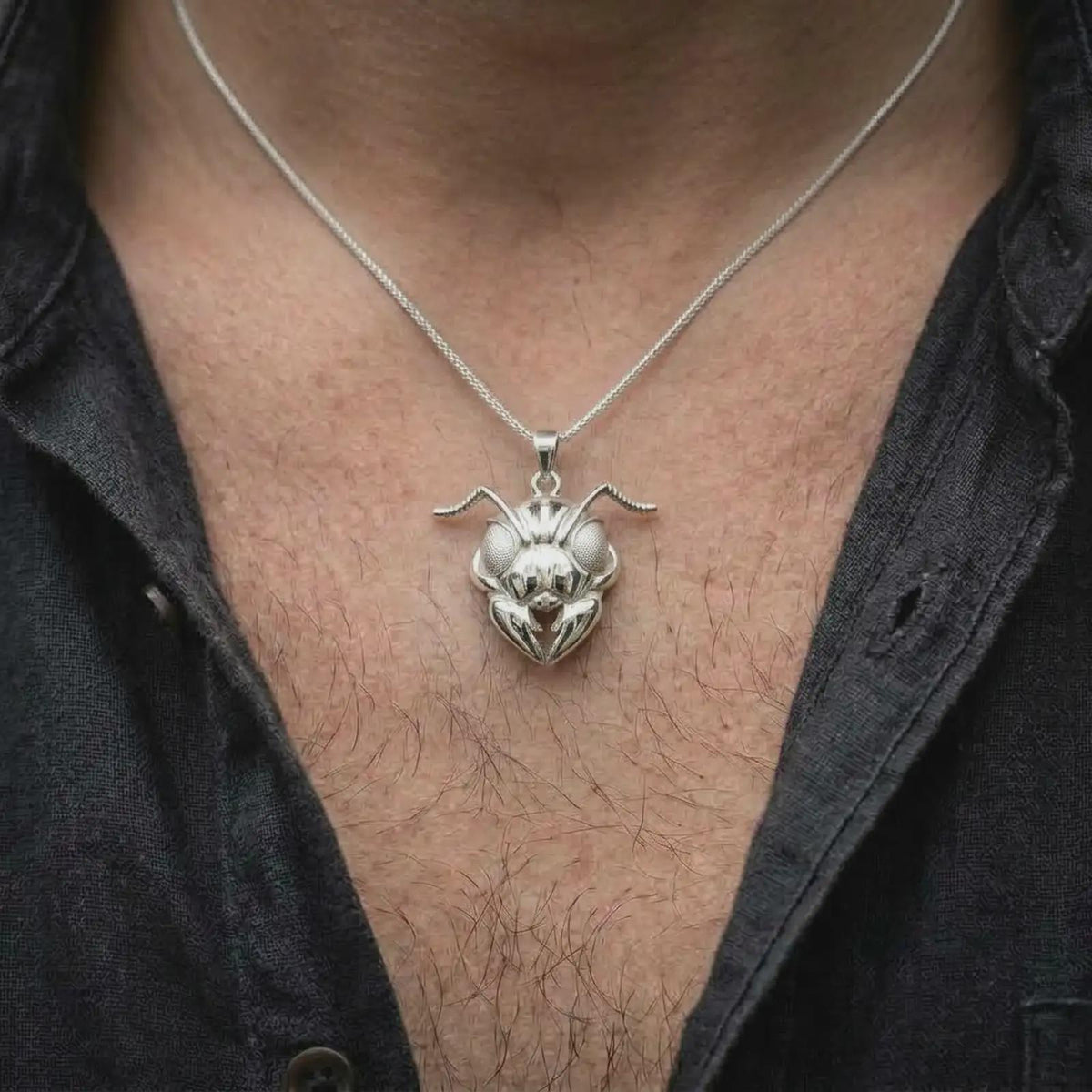 The polished silver ant pendant is worn naturally on the chest, showing the reflective insect head, prominent compound eyes, curved antennae, and detailed three-dimensional mandibles in a premium lifestyle image.