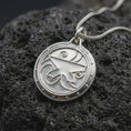 Load image into Gallery viewer, The polished silver fantasy RPG medallion is displayed on textured black volcanic rock, highlighting the central raised symbol, ornamental swirls, smooth circular frame, and detailed sterling silver relief.

