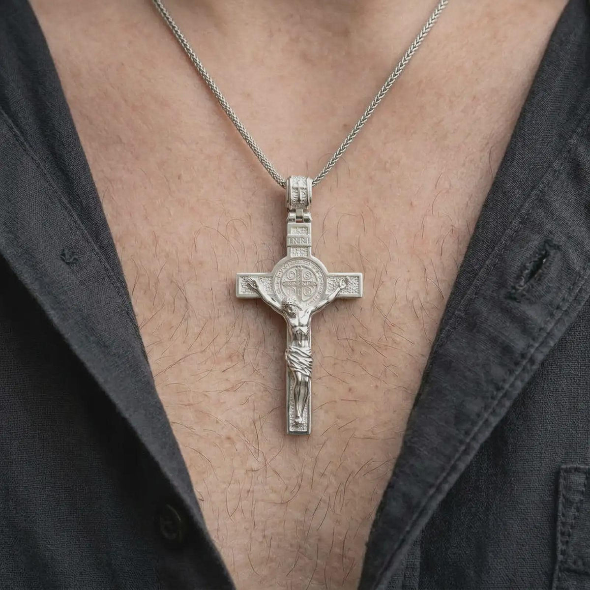 The polished silver Catholic crucifix is worn naturally on the chest, showing the sculpted Christ figure, Saint Benedict medal, structured cross silhouette, and detailed sterling silver finish.