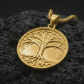 Load image into Gallery viewer, A gold plated Tree of Life pendant rests on rugged volcanic rock, showcasing the intricate Yggdrasil tree, flowing branches, detailed leaves, interconnected roots, and symbolic Norse-inspired medallion design.
