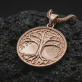 Load image into Gallery viewer, The rose gold plated Tree of Life necklace is arranged on black volcanic rock, emphasizing the raised tree silhouette, delicate leaf details, spreading branches, sculpted roots, and refined circular pendant design.
