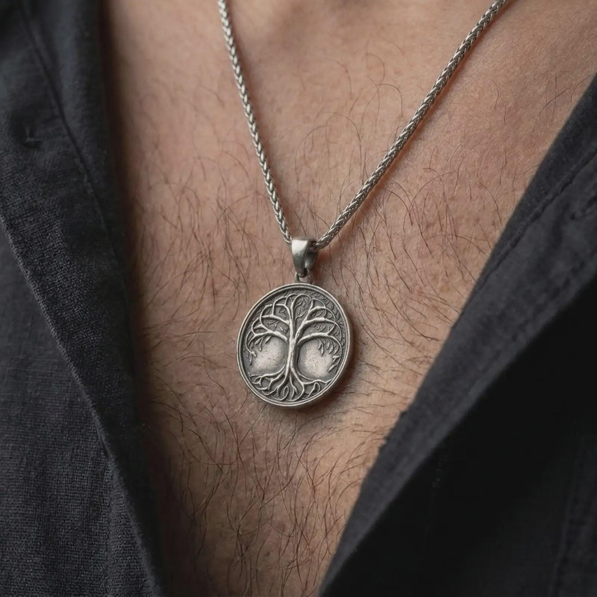An oxidized sterling silver Yggdrasil pendant is worn on the chest, displaying the circular Tree of Life medallion, dark recessed background, intricate branches, leaves, and intertwined roots in a close-up lifestyle photograph.