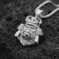 Load image into Gallery viewer, A polished sterling silver gorilla samurai pendant displayed on dark volcanic rock, highlighting its fierce expression, sculpted facial features, ornamental helmet, and intricate metalwork.
