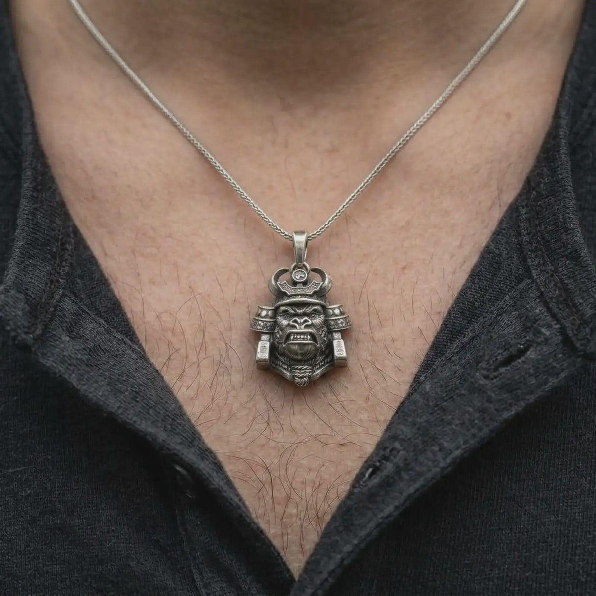 An oxidized sterling silver gorilla samurai necklace worn on a man's chest, displaying the fierce gorilla face, curved helmet horns, intricate Japanese-inspired armor, and rugged men's jewelry style.