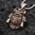 Load image into Gallery viewer, An bronze sterling silver King Gorilla Samurai pendant rests on black volcanic rock, featuring a fierce gorilla face, curved helmet horns, decorative crown, and detailed Japanese warrior armor.
