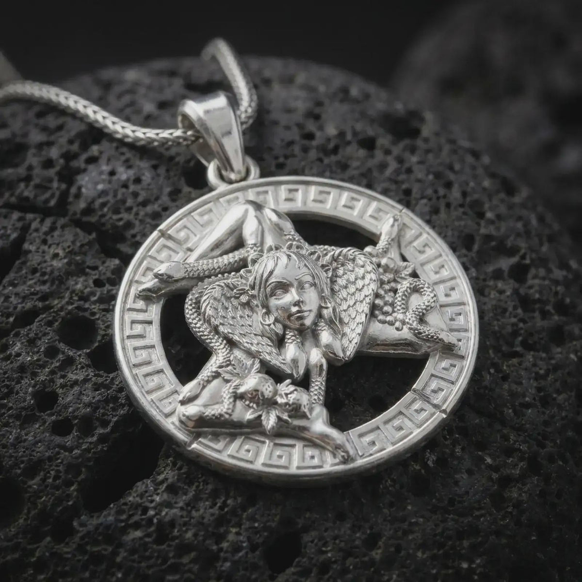 Polished sterling silver Sicilian Triskelion necklace on volcanic stone, showing the Medusa centerpiece, three-legged Trinacria design, and circular Greek key frame.