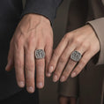 Load image into Gallery viewer, Oxidized sterling silver Crucifixion ring worn on the hand, showing Jesus Christ between the two thieves, three-cross Calvary scene, INRI lettering, and bold religious signet shape.
