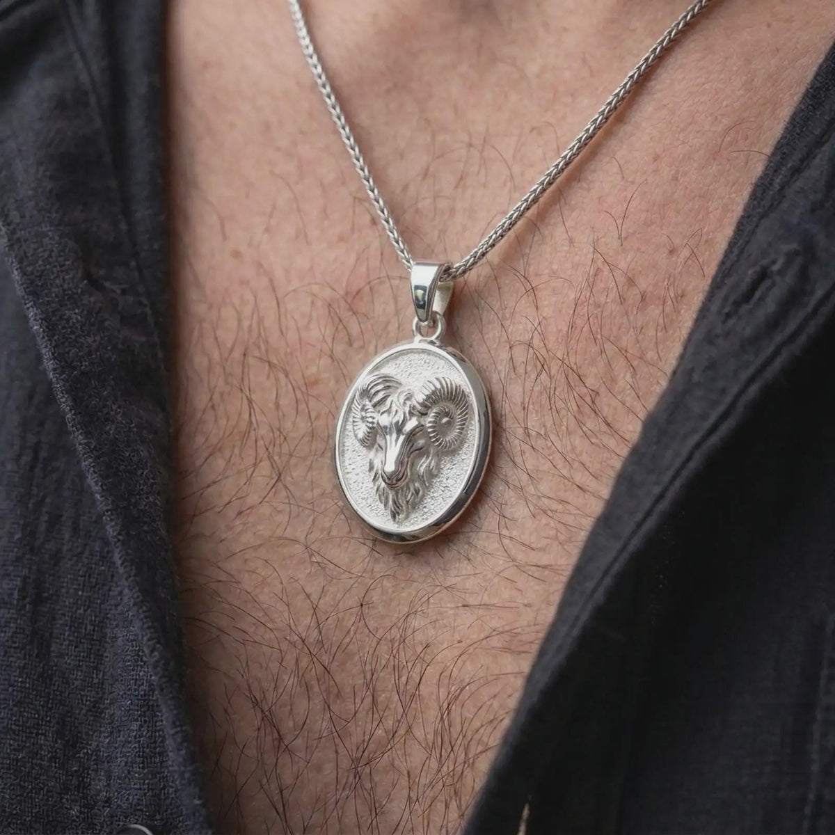 Polished silver ram head pendant worn on the chest, featuring detailed curled horns, sculpted facial features, and a distinctive Aries zodiac medallion.
