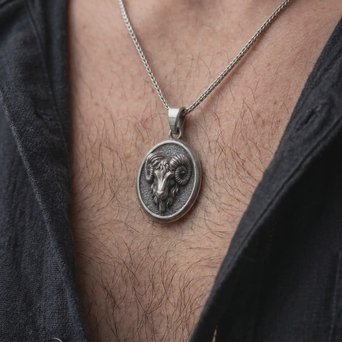 Oxidized sterling silver Aries necklace worn on the chest, showing the dimensional ram head, large curved horns, textured medallion, and bold zodiac jewelry design.