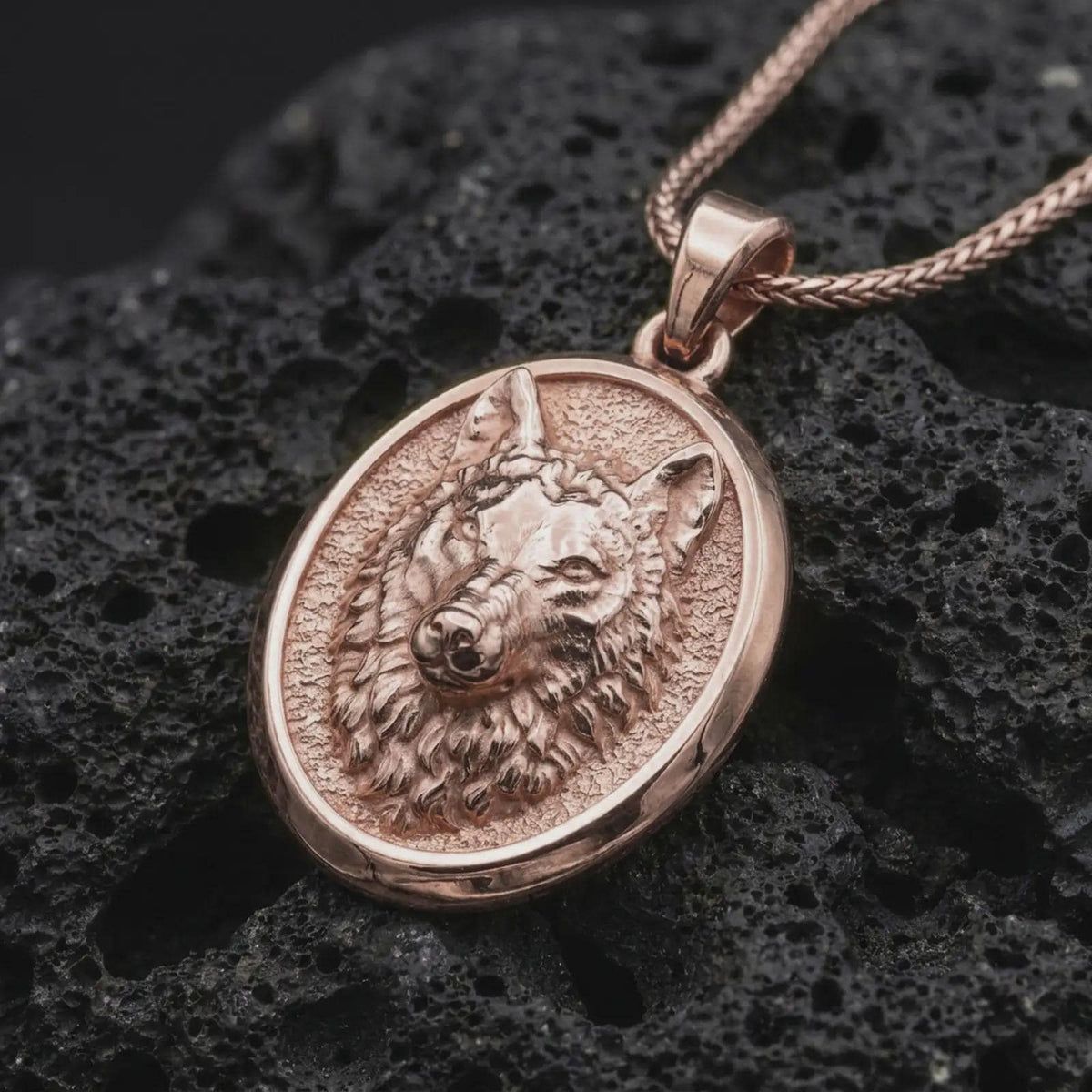 Rose gold plated wolf necklace displayed on textured volcanic stone, showcasing the sculpted wolf head, expressive eyes, layered fur, and distinctive oval pendant profile.