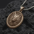 Load image into Gallery viewer, Bronze wolf head pendant on black volcanic rock, featuring a sculpted wolf face, detailed fur, pointed ears, textured background, and oval medallion frame.
