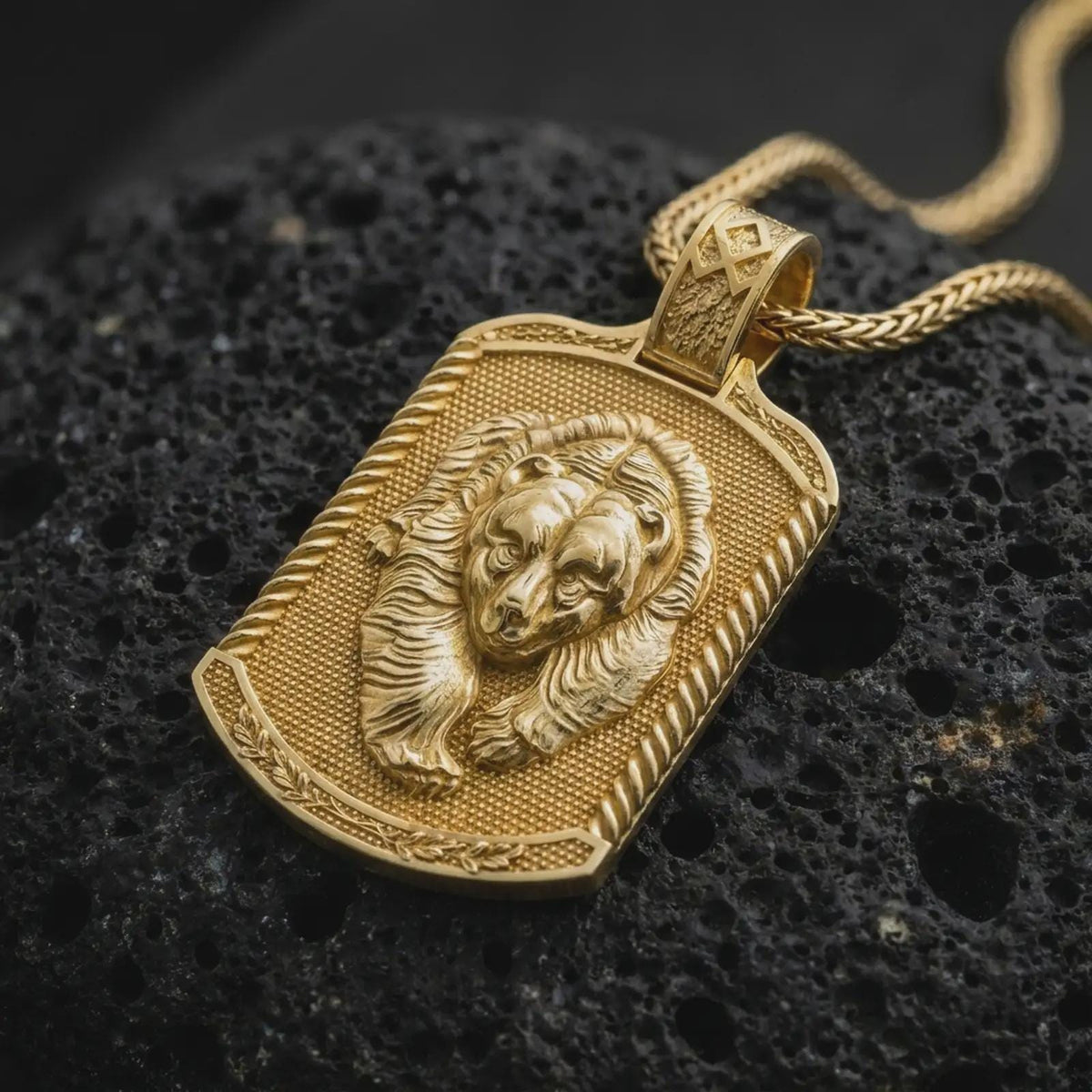 Gold plated bear family pendant resting on black volcanic rock, featuring a parent bear and cub nestled together with sculpted fur, textured background, and bold rectangular medallion frame.