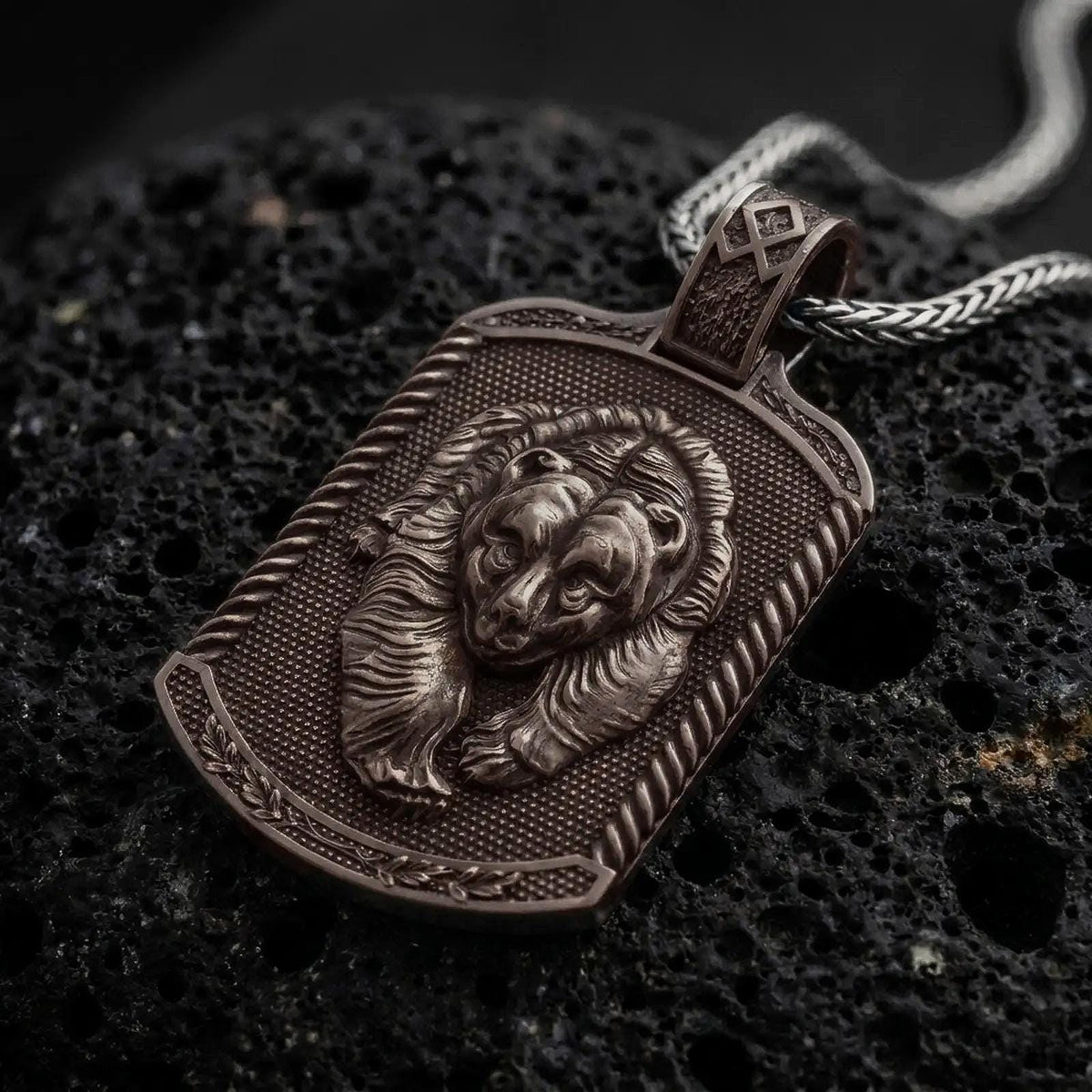 Bronze bear and cub pendant on black volcanic rock, featuring two sculpted bear faces, detailed fur, textured dog tag background, and decorative border.