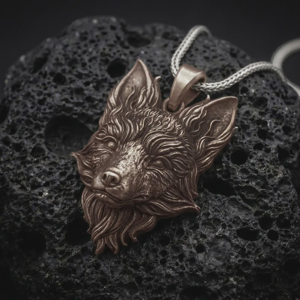 Bronze fox head pendant on black volcanic rock, featuring pointed ears, a narrow sculpted muzzle, expressive eyes, and detailed flowing fur.
