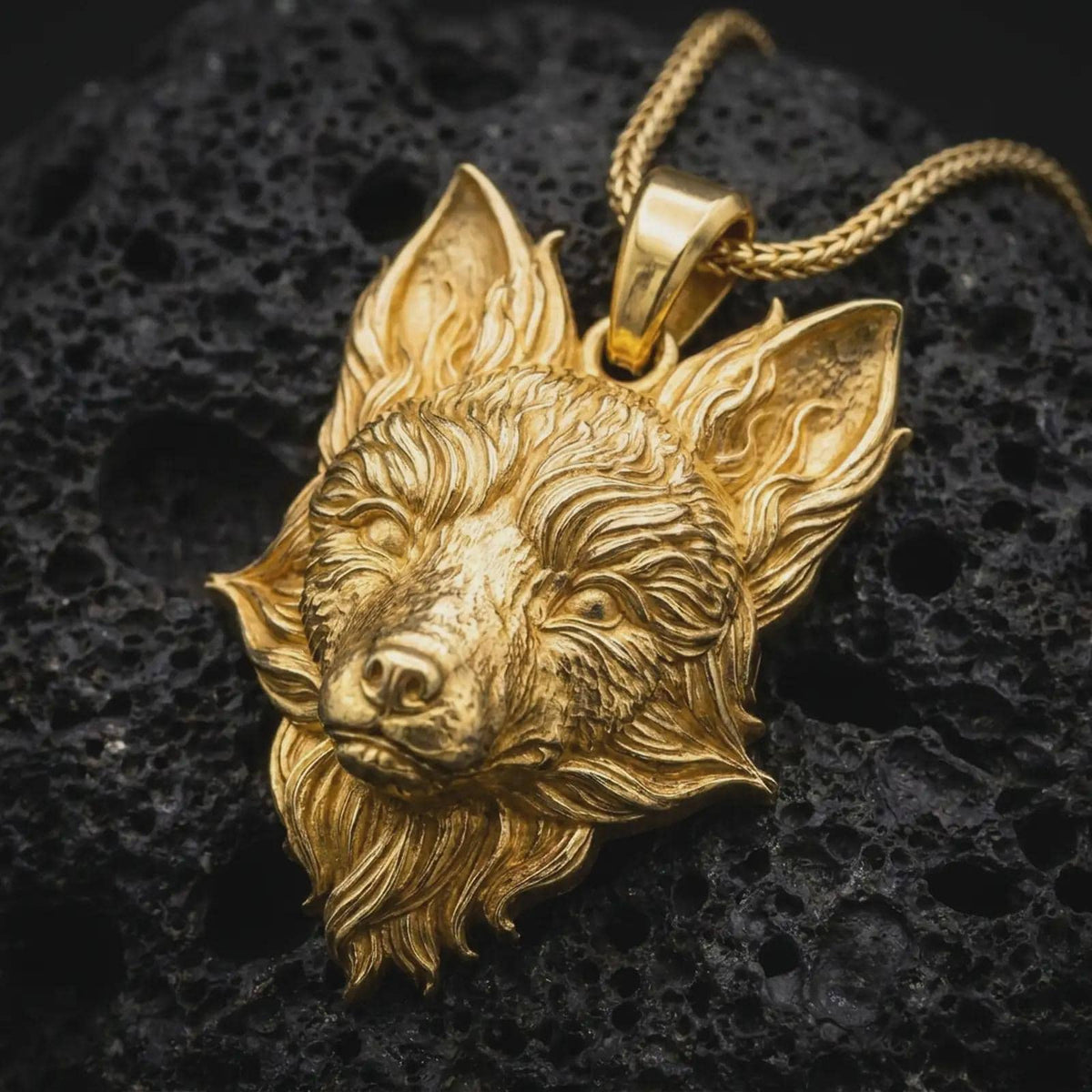 Gold plated fox head pendant resting on black volcanic rock, featuring a detailed fox portrait, pointed ears, sculpted muzzle, and bold woodland-inspired jewelry design.