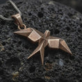 Load image into Gallery viewer, Bronze origami swallow pendant on black volcanic rock, featuring sharp geometric folds, pointed wings, and a faceted flying bird silhouette.
