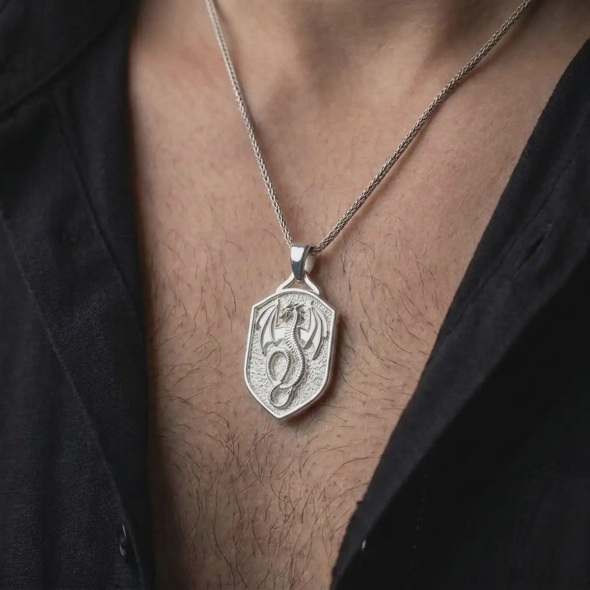 Polished silver coiled dragon pendant worn on the chest, featuring detailed wings, scaled serpentine body, curled tail, and a distinctive mythical creature shield design.