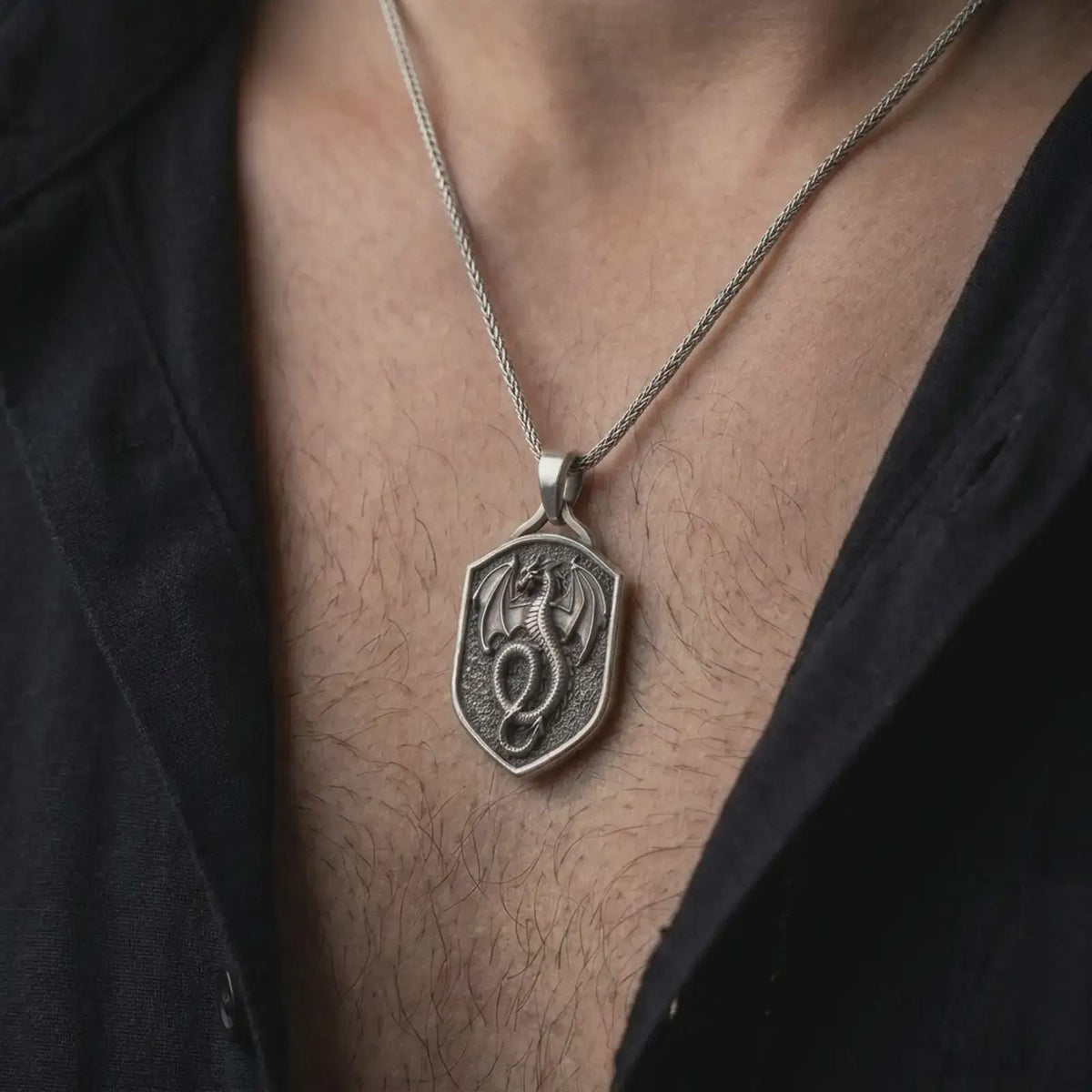 Oxidized sterling silver dragon shield necklace worn on the chest, showing the coiled winged dragon, textured shield background, and bold medieval fantasy pendant profile.