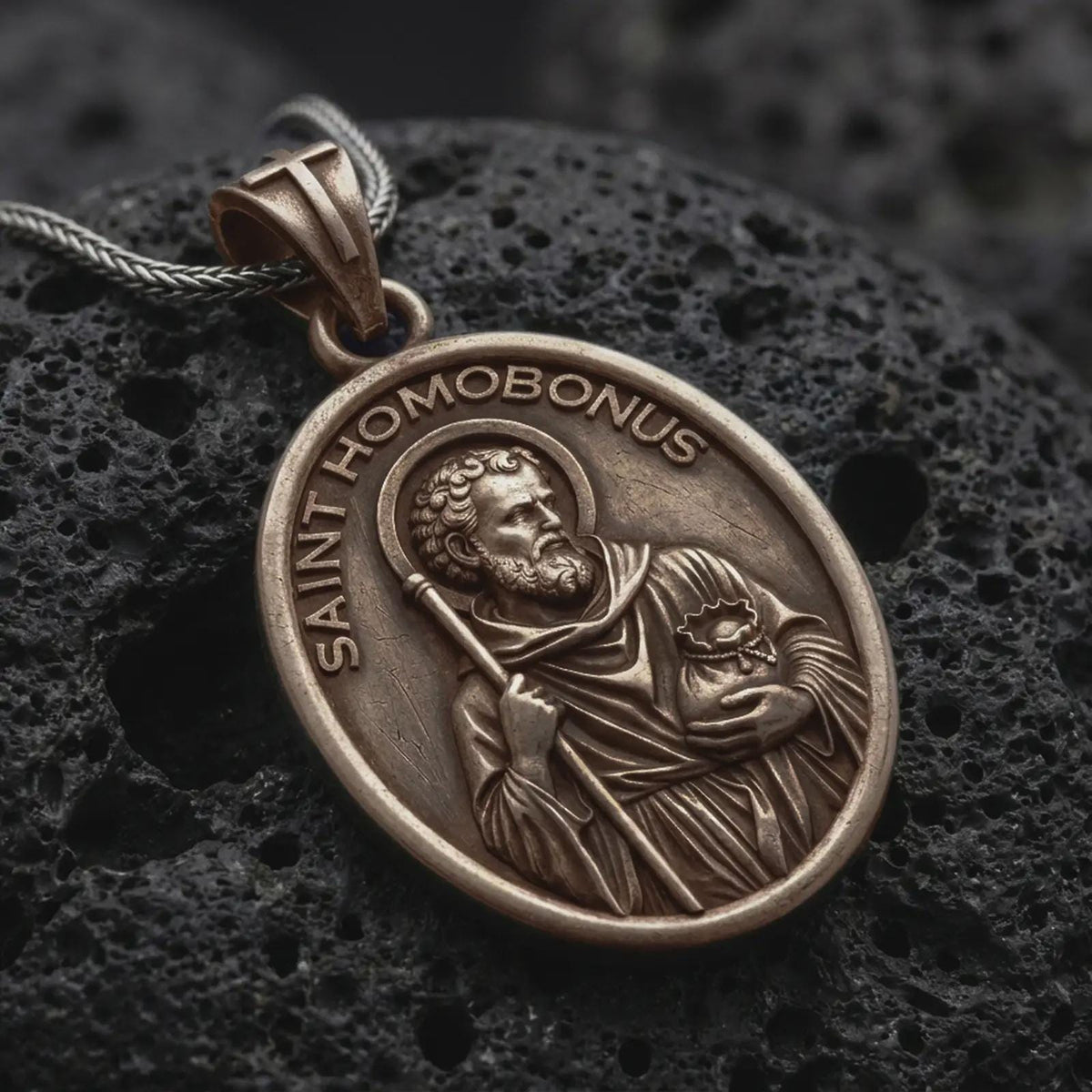 Bronze sterling silver Saint Homobonus medal necklace on black volcanic rock, featuring the haloed Catholic saint holding a staff with SAINT HOMOBONUS lettering.