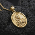 Load image into Gallery viewer, Gold plated Saint Homobonus medal resting on black volcanic rock, featuring the patron saint associated with merchants and business owners in a detailed Catholic pendant design.
