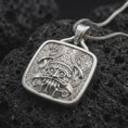 Load image into Gallery viewer, Polished sterling silver Tlaloc necklace displayed on dark volcanic stone, highlighting the Mexica rain god face, ceremonial headdress details, fangs, and geometric relief.
