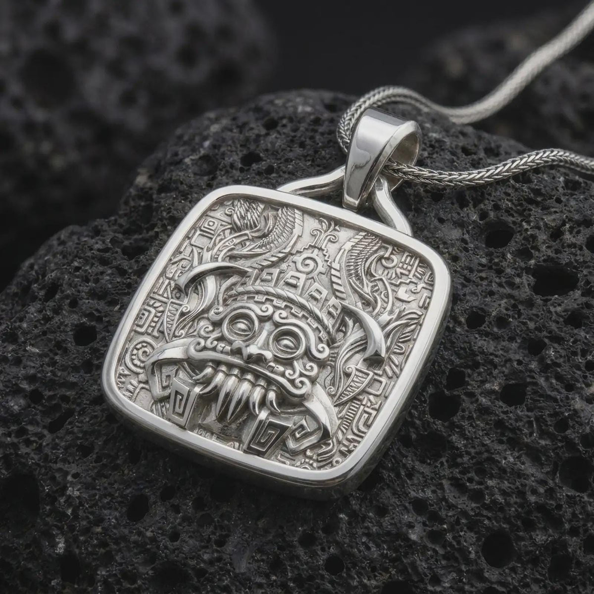 Polished sterling silver Tlaloc necklace displayed on dark volcanic stone, highlighting the Mexica rain god face, ceremonial headdress details, fangs, and geometric relief.