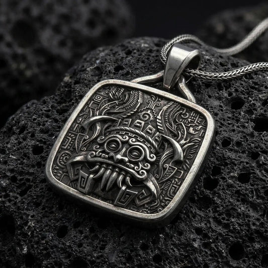 Oxidized sterling silver Tlaloc pendant on black volcanic rock, featuring ringed eyes, prominent fangs, curled facial details, and intricate Aztec geometric patterns.