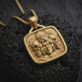 Load image into Gallery viewer, Gold plated Aztec jaguar necklace on black volcanic rock, featuring a sculpted ceremonial face surrounded by skulls, feline imagery, feathered details, and ancient Mesoamerican patterns.
