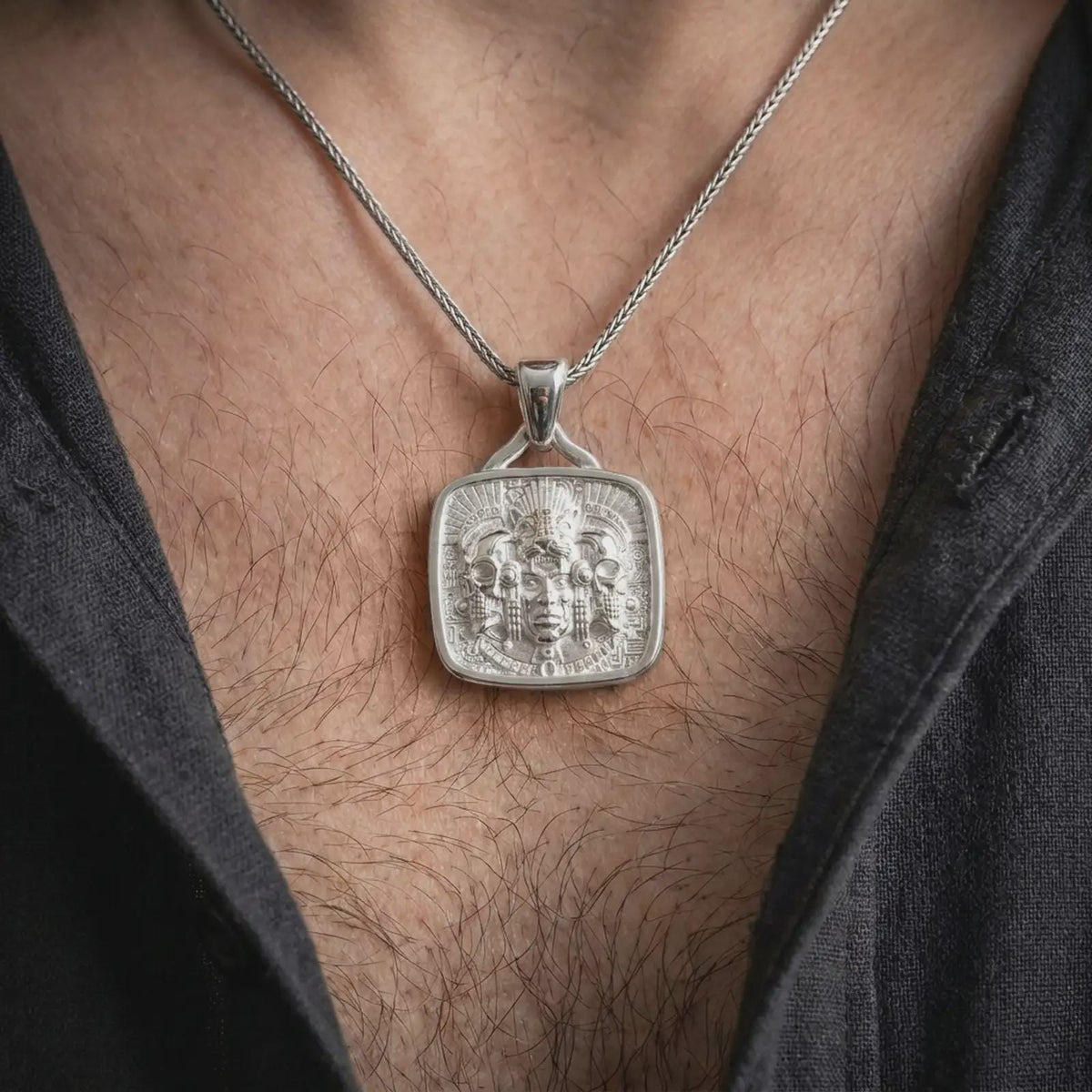 Polished silver Aztec warrior pendant worn on the chest, featuring detailed jaguar symbolism, flanking skulls, feather ornaments, and a bold square statement medallion.