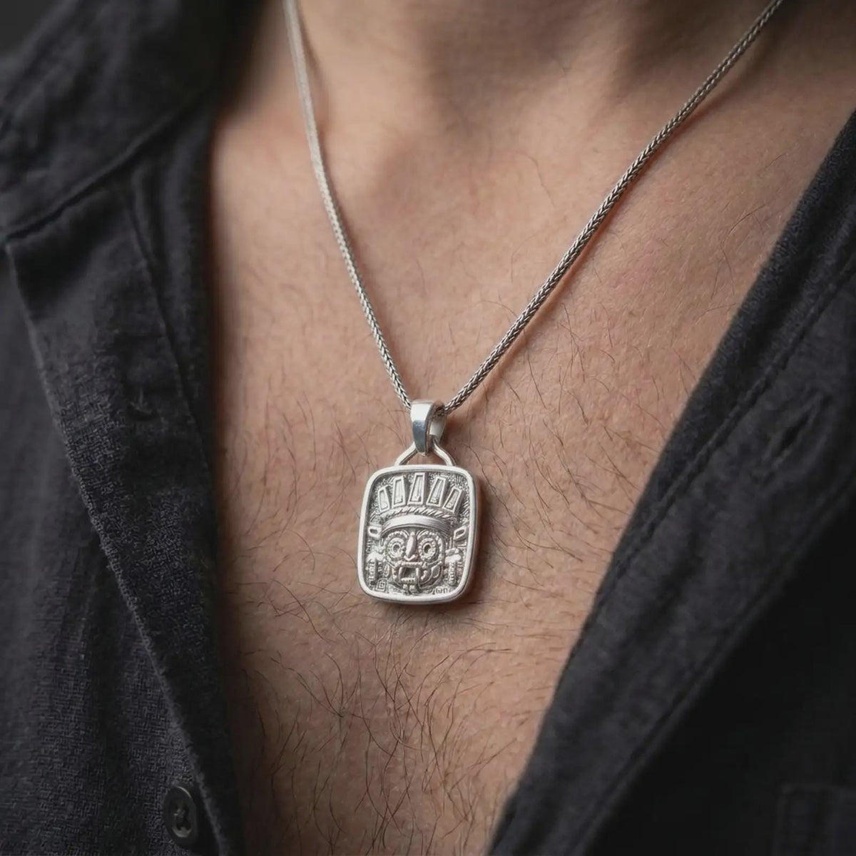 Polished silver Aztec Tlaloc pendant worn on the chest, featuring the iconic rain deity face, elaborate headdress, geometric patterns, and bold Mesoamerican styling.