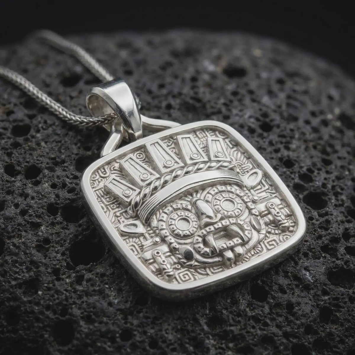 Polished sterling silver Tlaloc necklace displayed on dark volcanic stone, highlighting the rain god mask, circular eyes, sculpted facial details, and elaborate Mexica-inspired headdress.