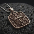 Load image into Gallery viewer, Bronze Tlaloc pendant on black volcanic rock, featuring iconic goggle eyes, fanged mouth, ceremonial headdress, and detailed Aztec geometric patterns.
