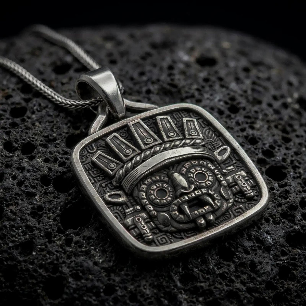 Oxidized sterling silver Tlaloc pendant on black volcanic rock, featuring iconic goggle eyes, fanged mouth, ceremonial headdress, and detailed Aztec geometric patterns.