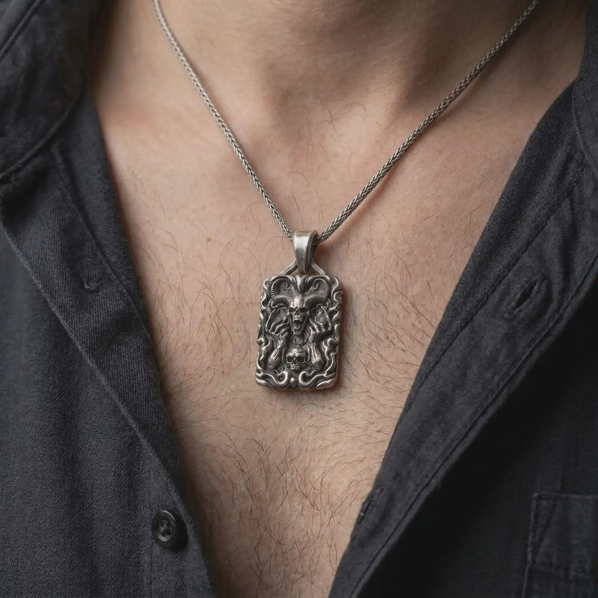 Oxidized sterling silver horned skull necklace worn on the chest, displaying the large curled horns, screaming skull, skeletal hands, and gothic flame details.