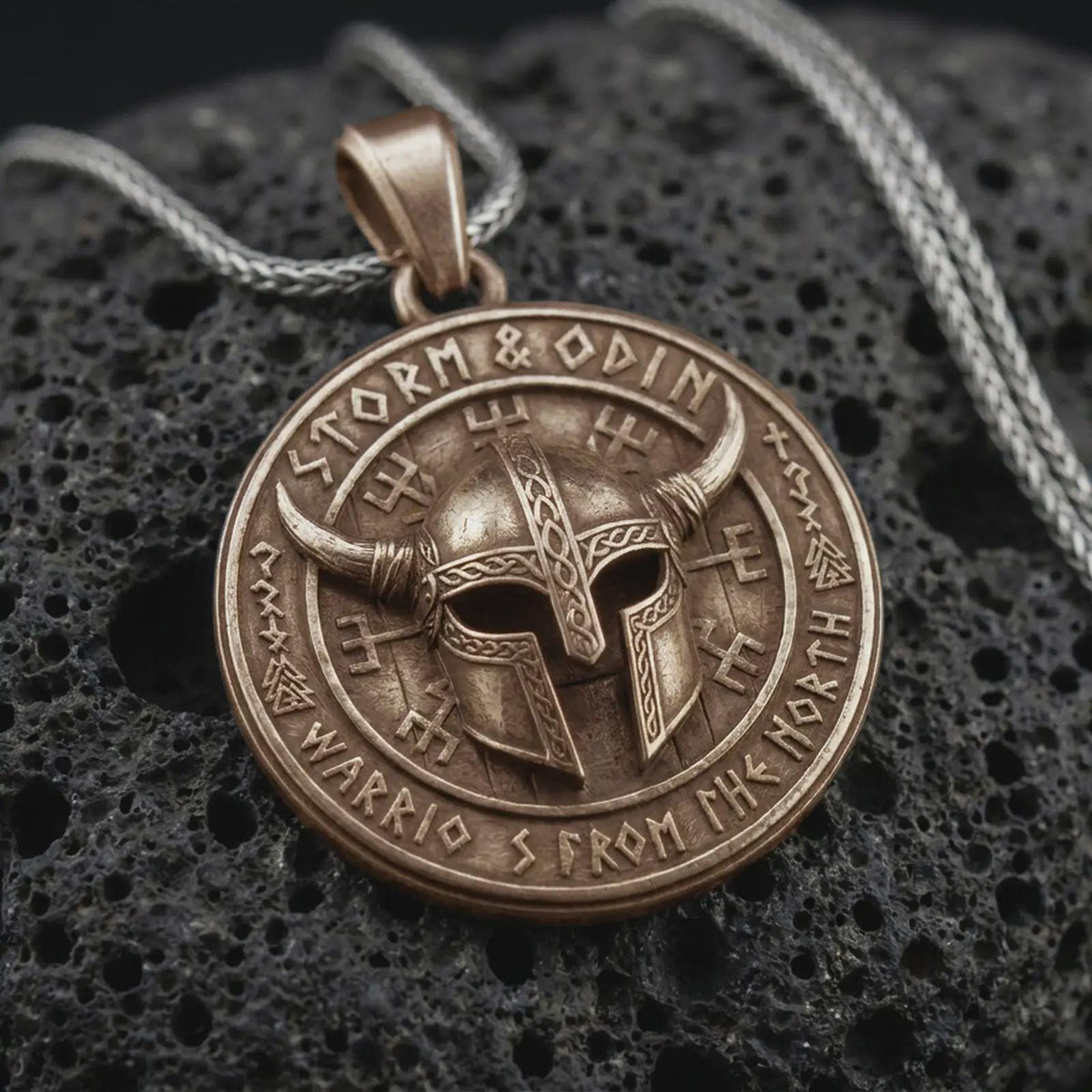 Bronze Viking helmet pendant on black volcanic rock, featuring a horned warrior helmet, Storm and Odin lettering, and Norse-inspired rune symbols.